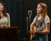 Confident girl singing and playing guitar with instructor